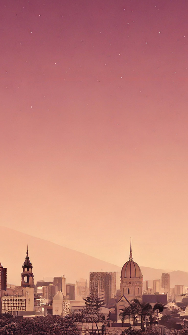 広大なピンクからオレンジへのグラデーションの空と、遠くに星がわずかに見える幻想的な風景。地平線近くには、ドームや尖塔を持つ建物が立ち並ぶ街並みと、その奥に薄く山脈のシルエットが見える。全体が暖かく落ち着いたトーンで描かれている。