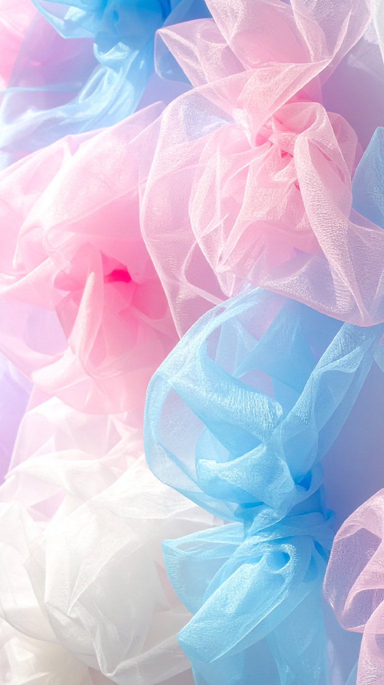 ピンク、水色、白の薄い布がパステル調で重なり合う抽象的なテクスチャ。