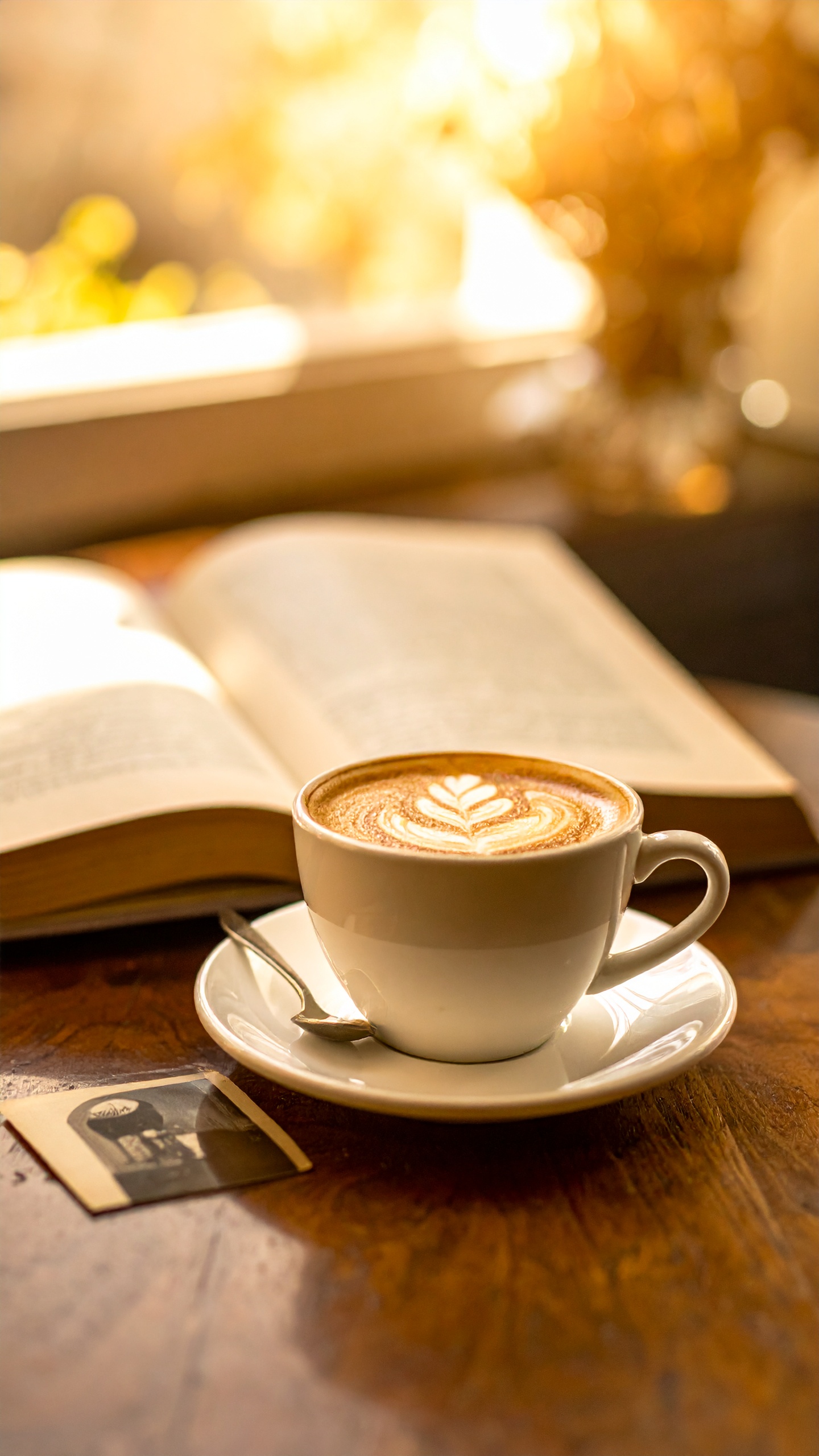 美しいラテアートが施された一杯のカフェラテと、その傍らに置かれた読みかけの本。窓から差し込む柔らかな琥珀色の光が、穏やかな午後のひとときを演出しています。