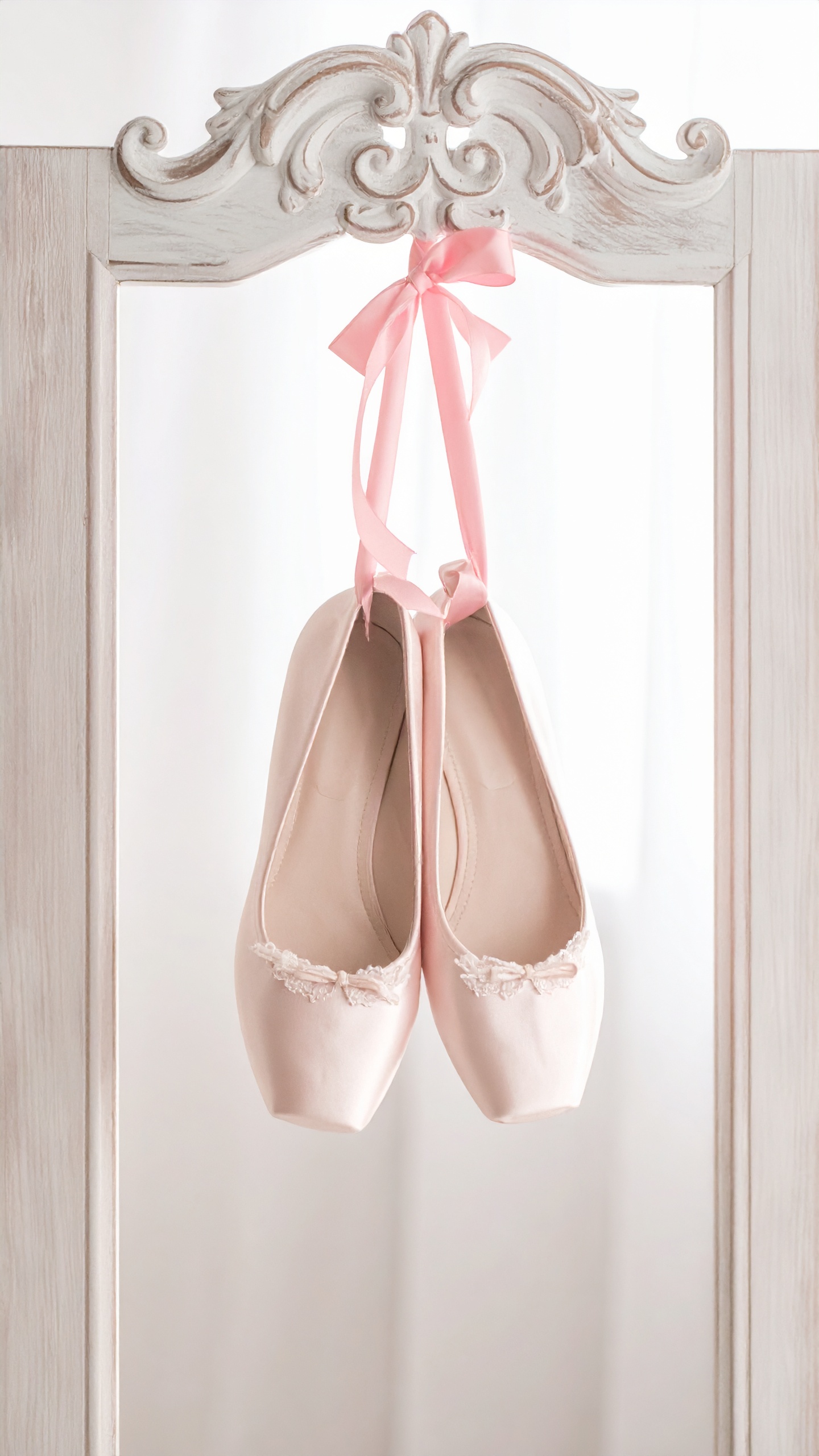装飾的な白いフレームに、ピンクのリボンで吊るされた淡い色のフラットシューズ。